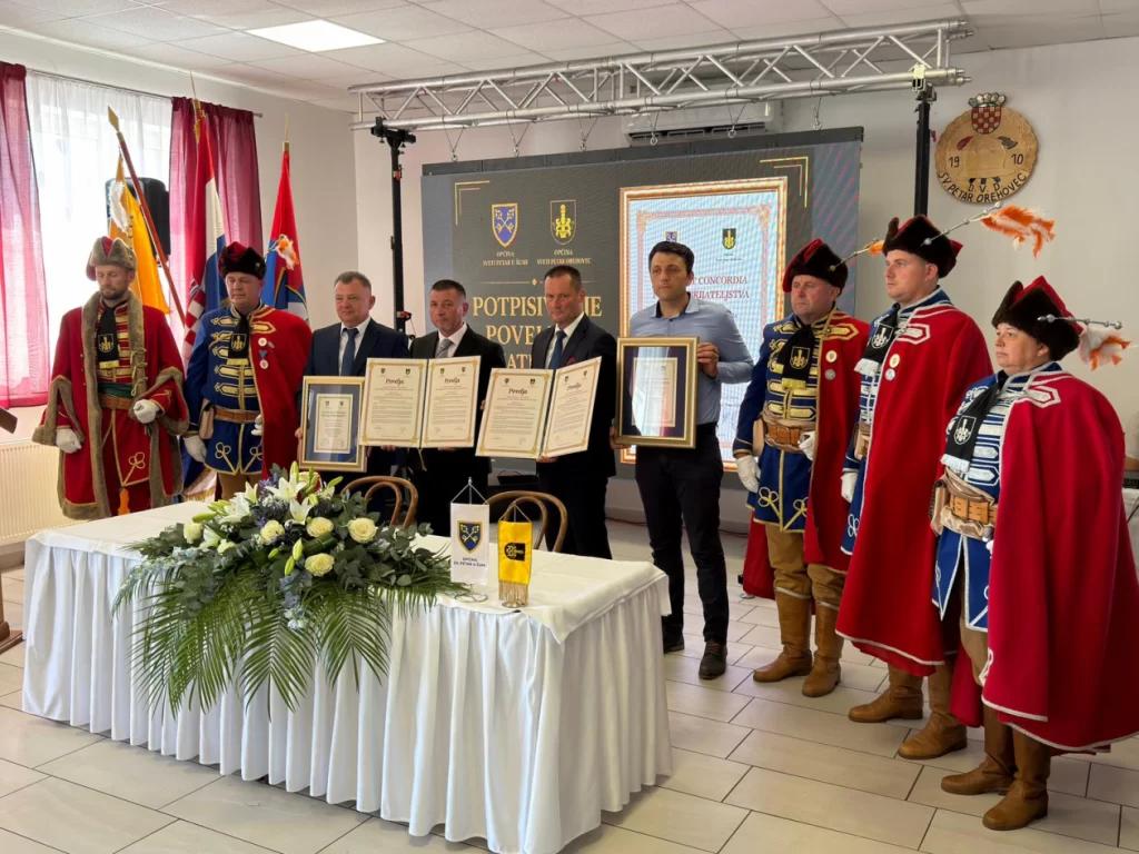 Potpisivanje Povelje prijateljstva u Sv. Petru Orehovcu, na fotografiji: načelnici Mario Bratulić i Josip Međan, predsjednici Općinskih vijeća Mario Gljuščić i Josip Međan te članovi Povijesne postrojbe Pukovnija Orehovečki, Izvor fotografije: Televizija Križevci